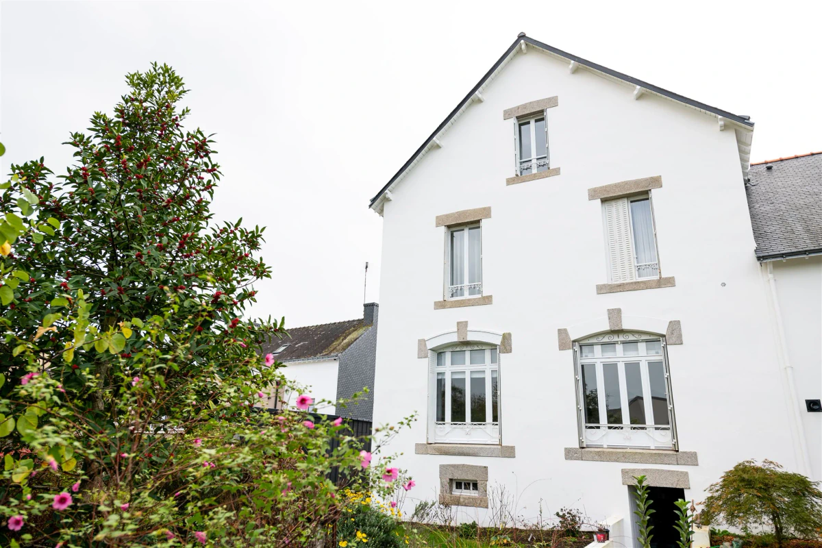 Maison repeinte en blanc après ravalement, jardin fleuri au premier plan