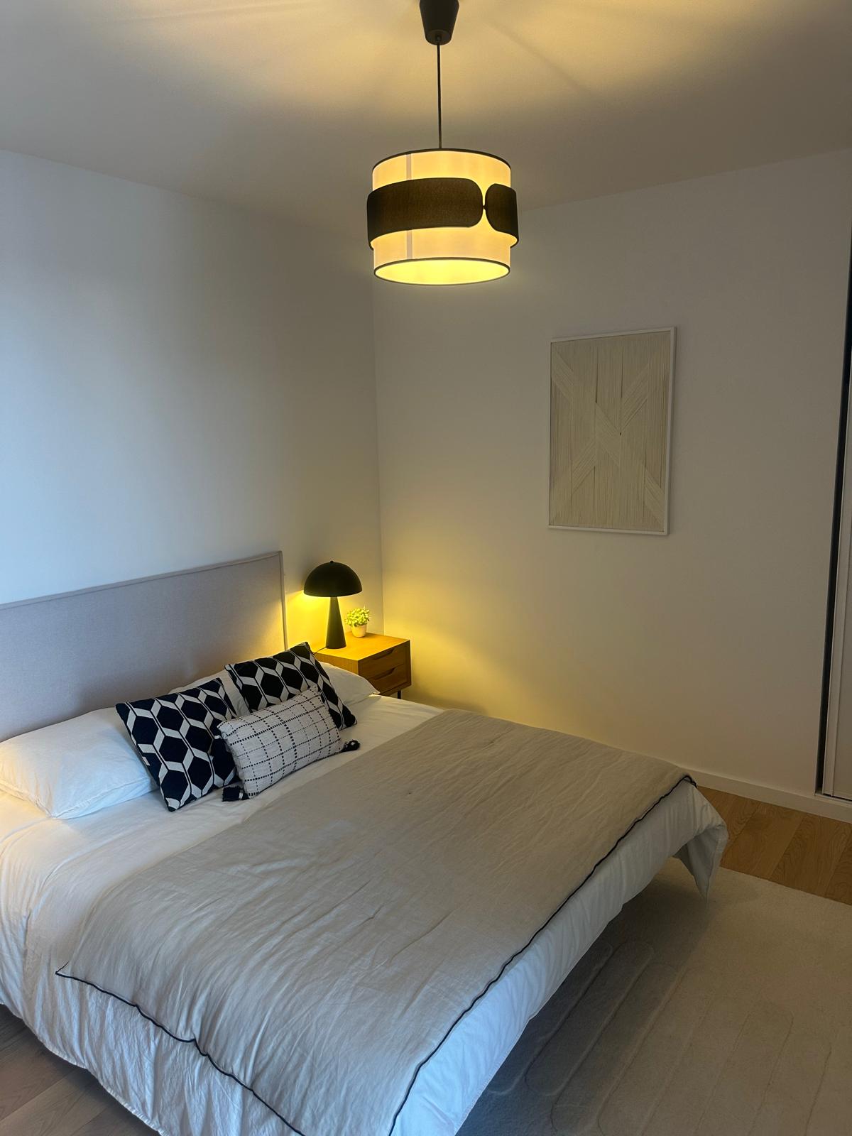 Chambre aux murs clairs, suspension et lampe de chevet allumées