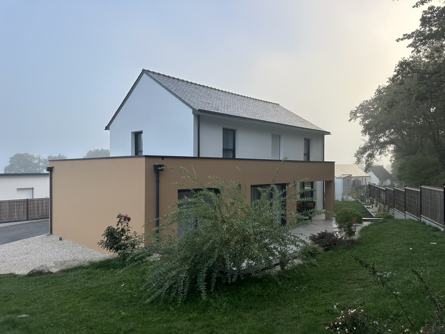 Maison contemporaine aux façades blanches et volume en enduit ocre, vue depuis le jardin